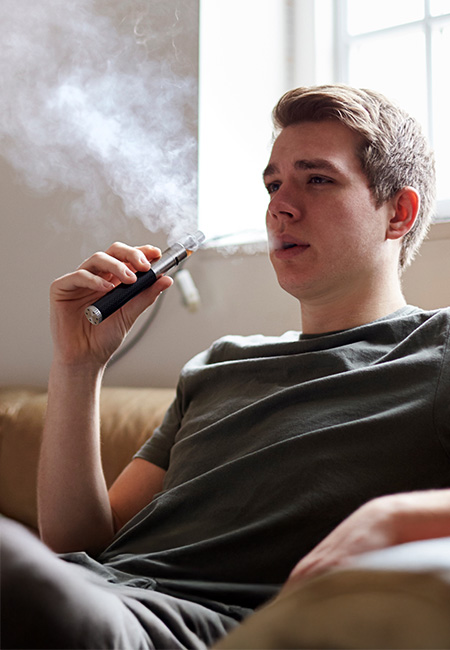 Young person vapes in his living room.