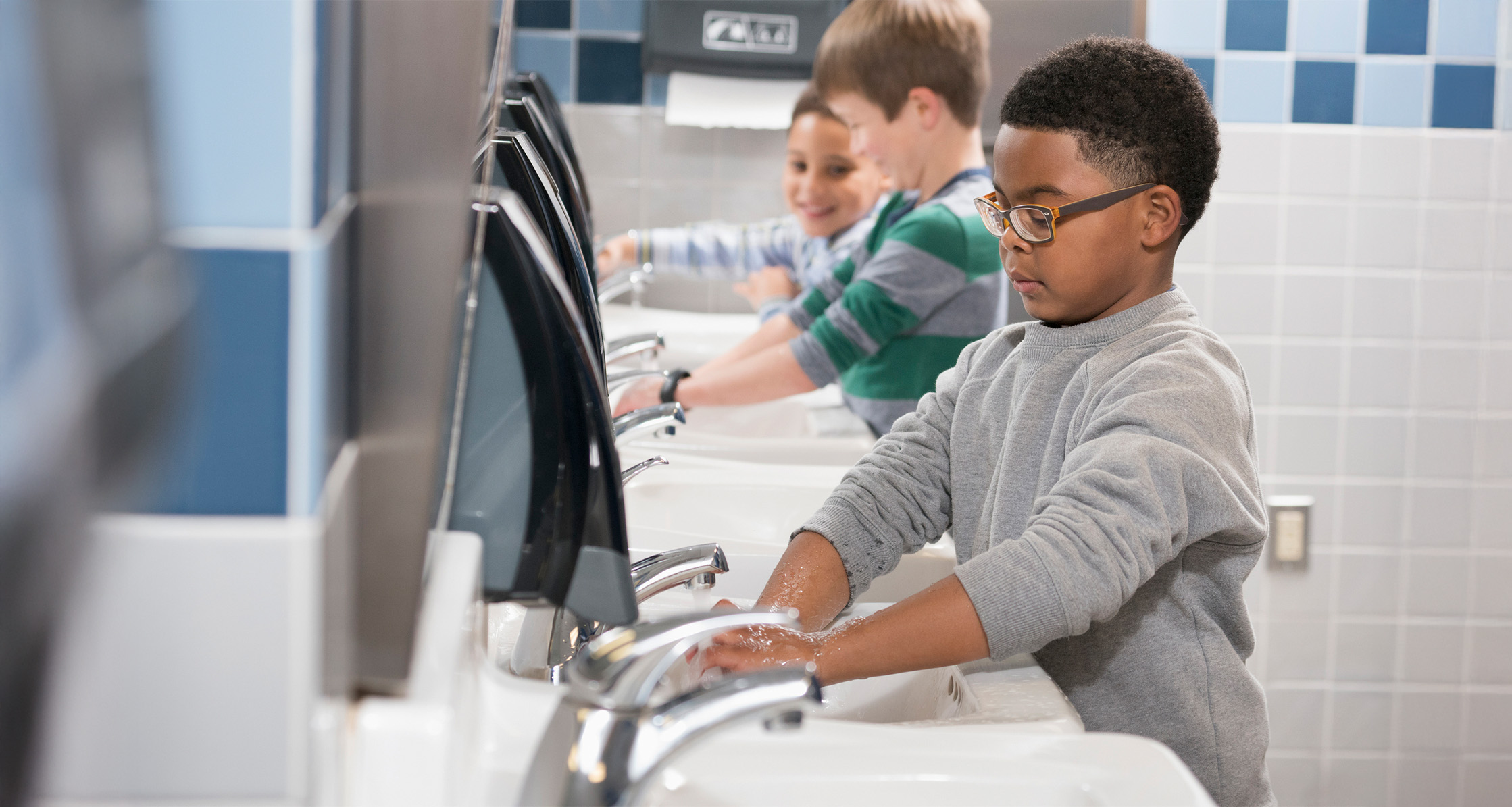 Elementary students wash their hands in school bathroom.