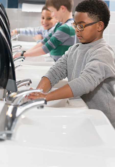 Elementary students wash their hands in school bathroom.