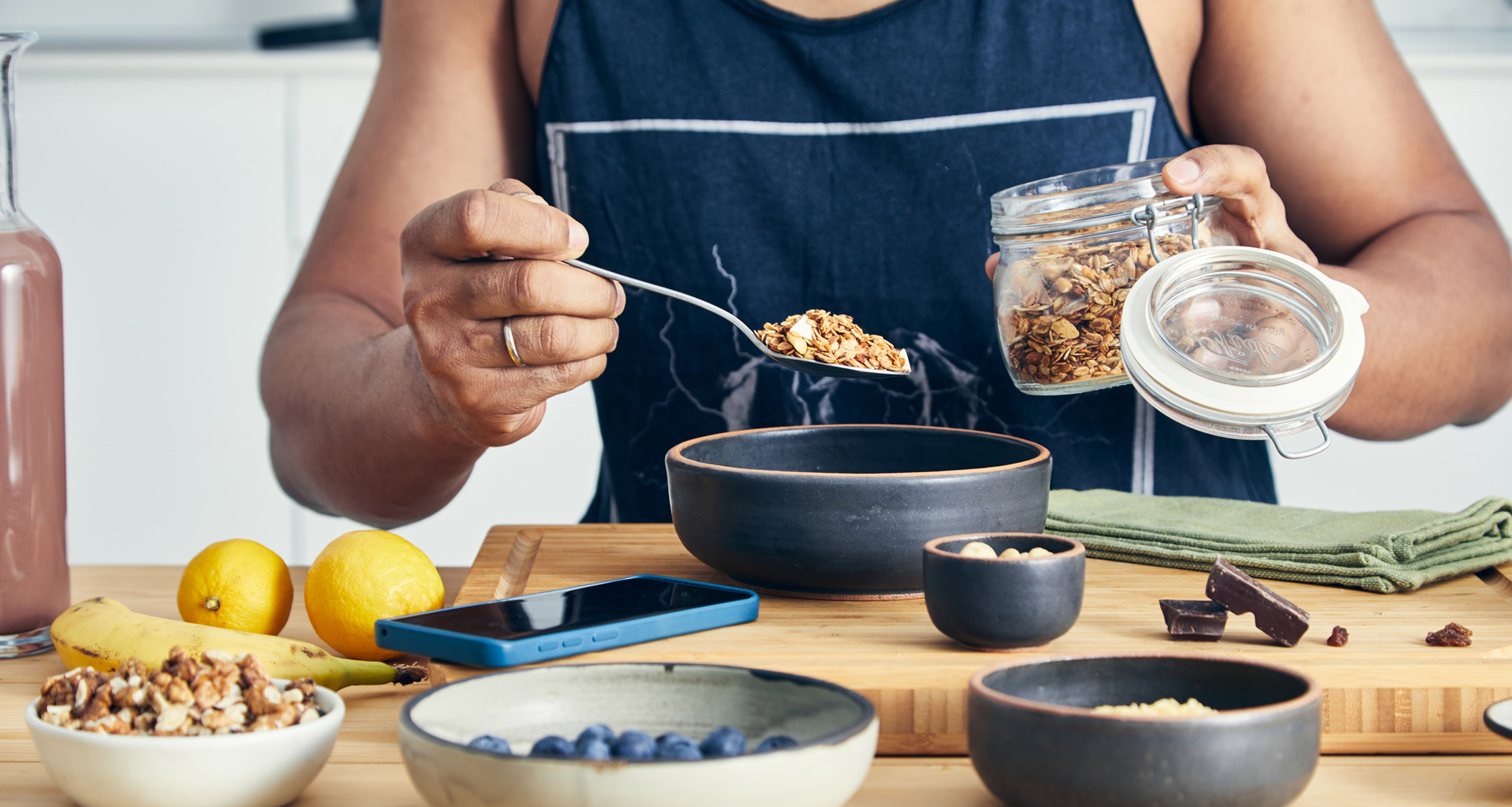 Person prepares a healthy breakfast with fruit, nuts, and granola.