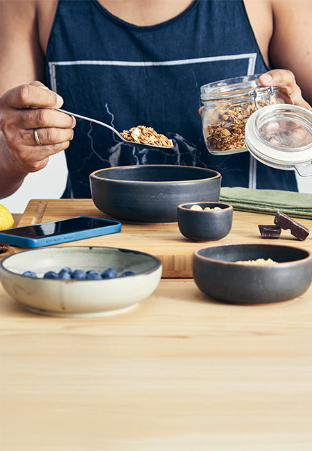Person prepares a healthy breakfast with fruit, nuts, and granola.