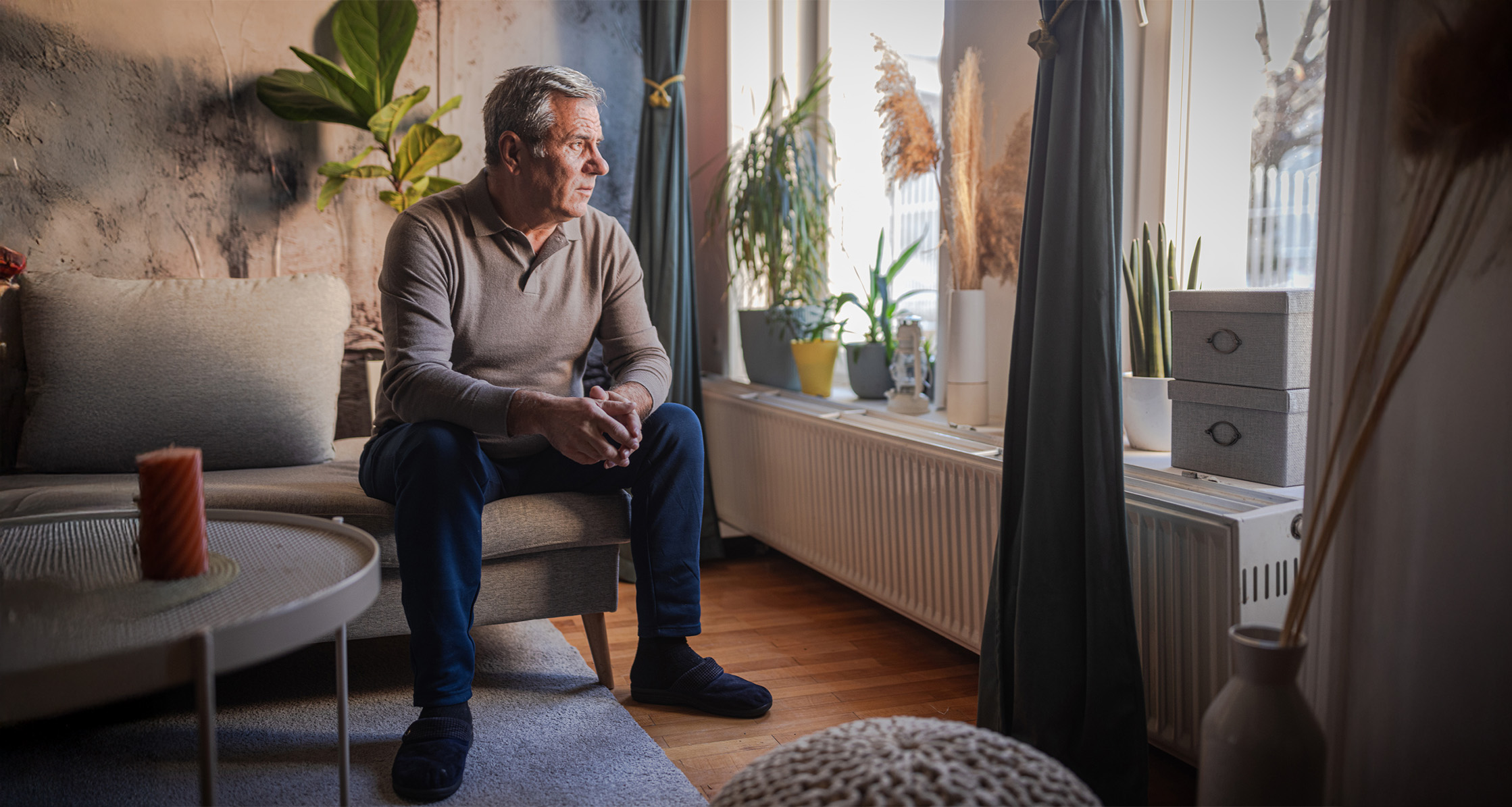 Older man sits indoors, looking out the window thoughtfully.