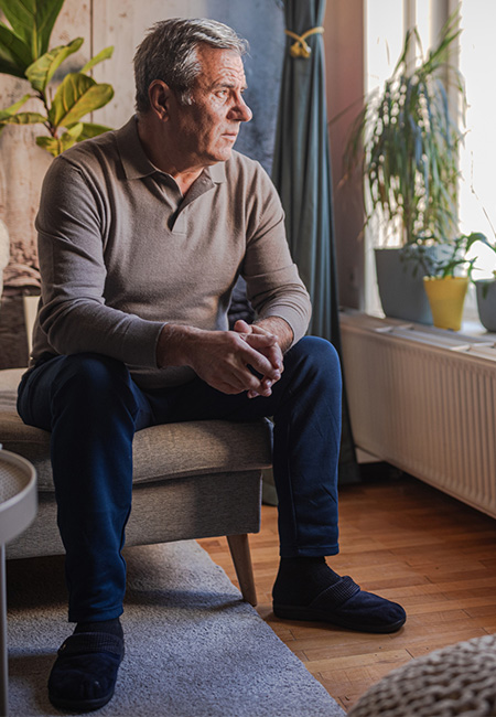 Older man sits indoors, looking out the window thoughtfully.