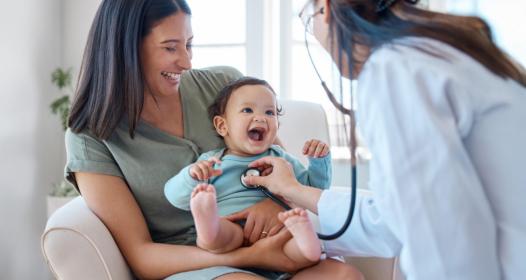 Pediatrician checks infant sitting in mom’s lap with a stethoscope.