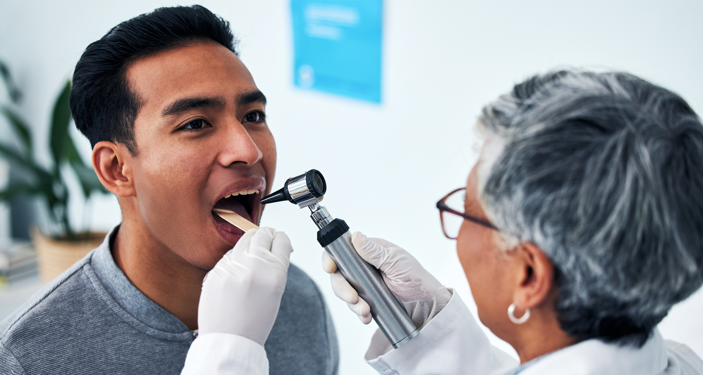 A health care provider consults with a man in a hospital and examines his throat.