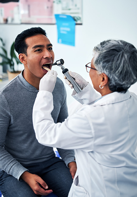 A health care provider consults with a man in a hospital and examines his throat.