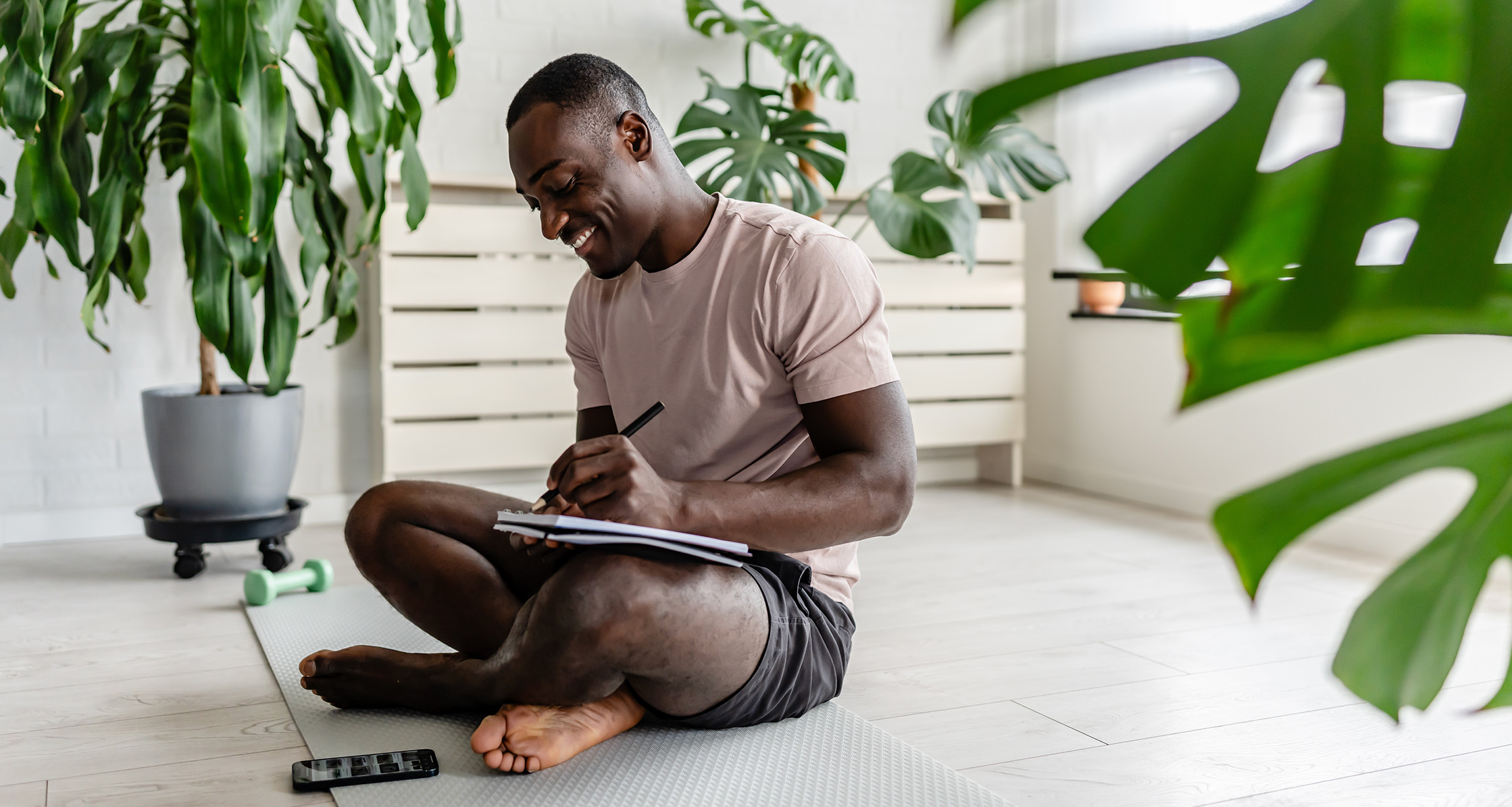 A man sitting on a yoga mat and journaling in a notebook.