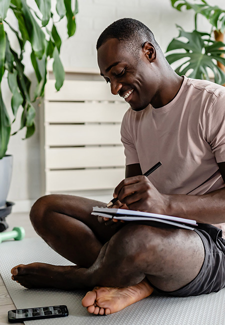 A man sitting on a yoga mat and journaling in a notebook.