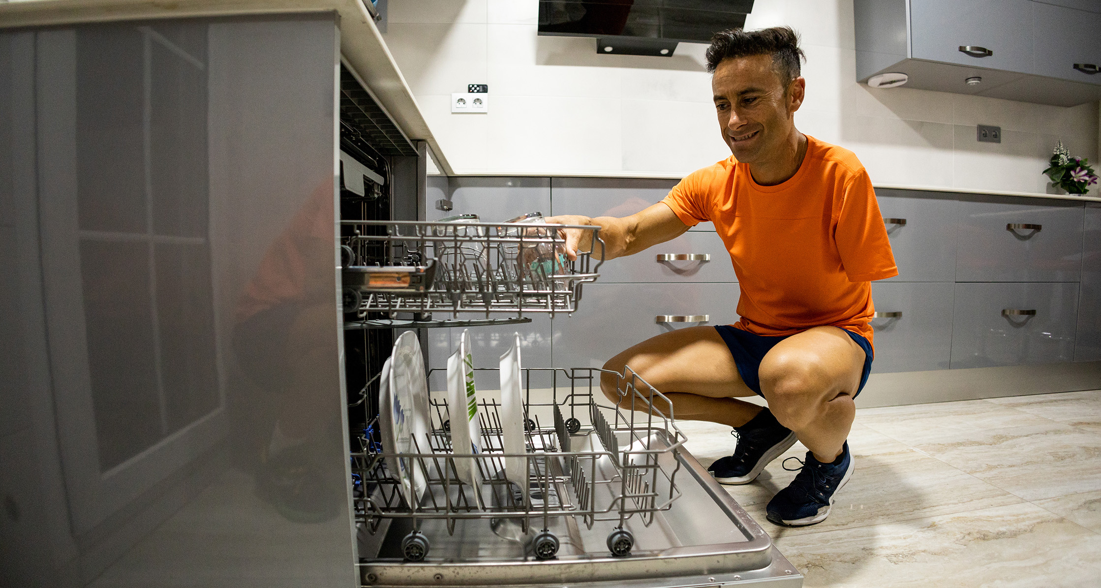 A disabled veteran squats to load a dishwasher.