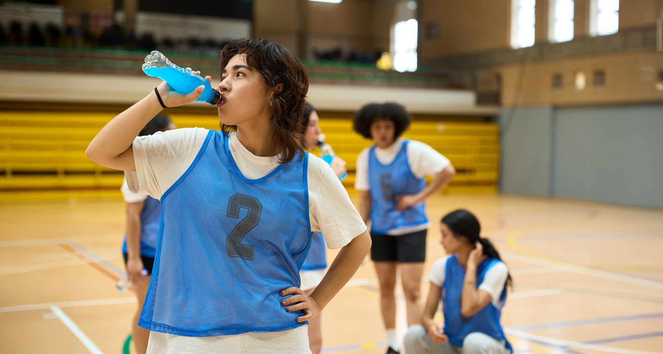 Teen drinks energy drink on basketball court.