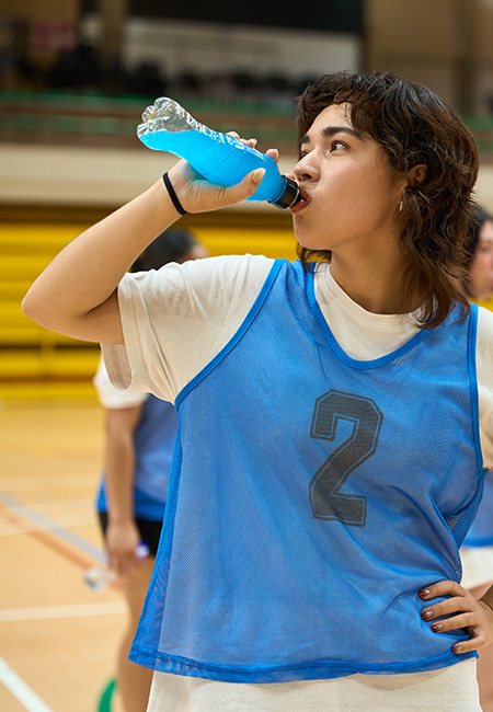 Teen drinks energy drink on basketball court.