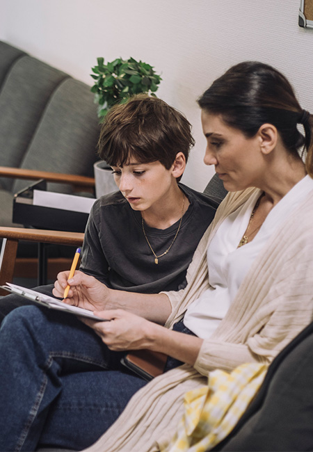 A mother with her son in urgent care waiting room, fills out paperwork.
