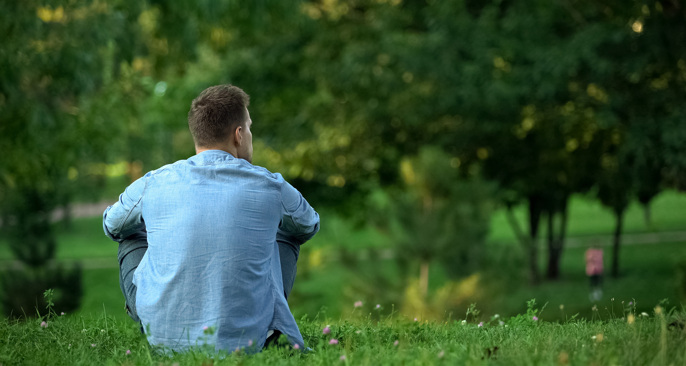Person sitting alone in a park reflecting in a quiet green space.
