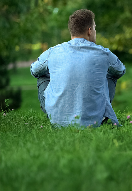 Person sitting alone in a park reflecting in a quiet green space.