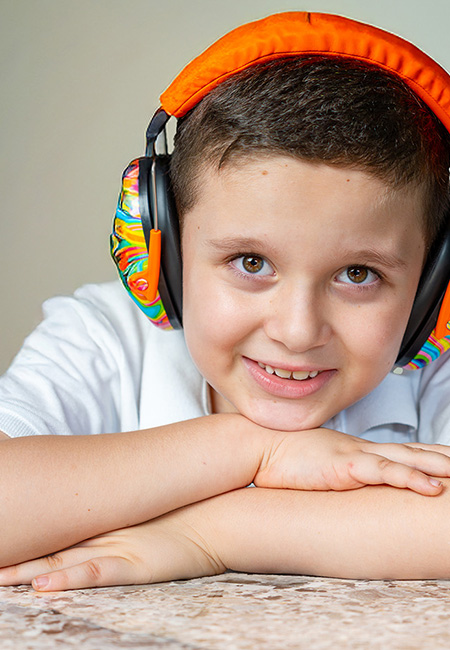 Autistic boy smiling with noise-canceling headphones for sensory comfort.