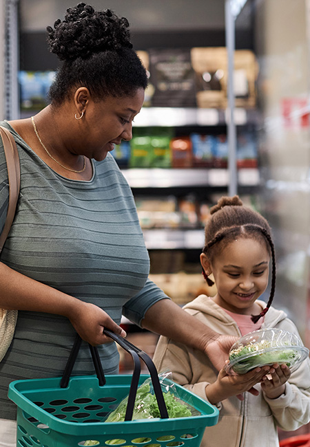 Mother shopping with daughter buying vegetables.
