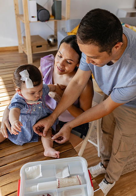 Parents applying bandage on baby daughter’s leg.