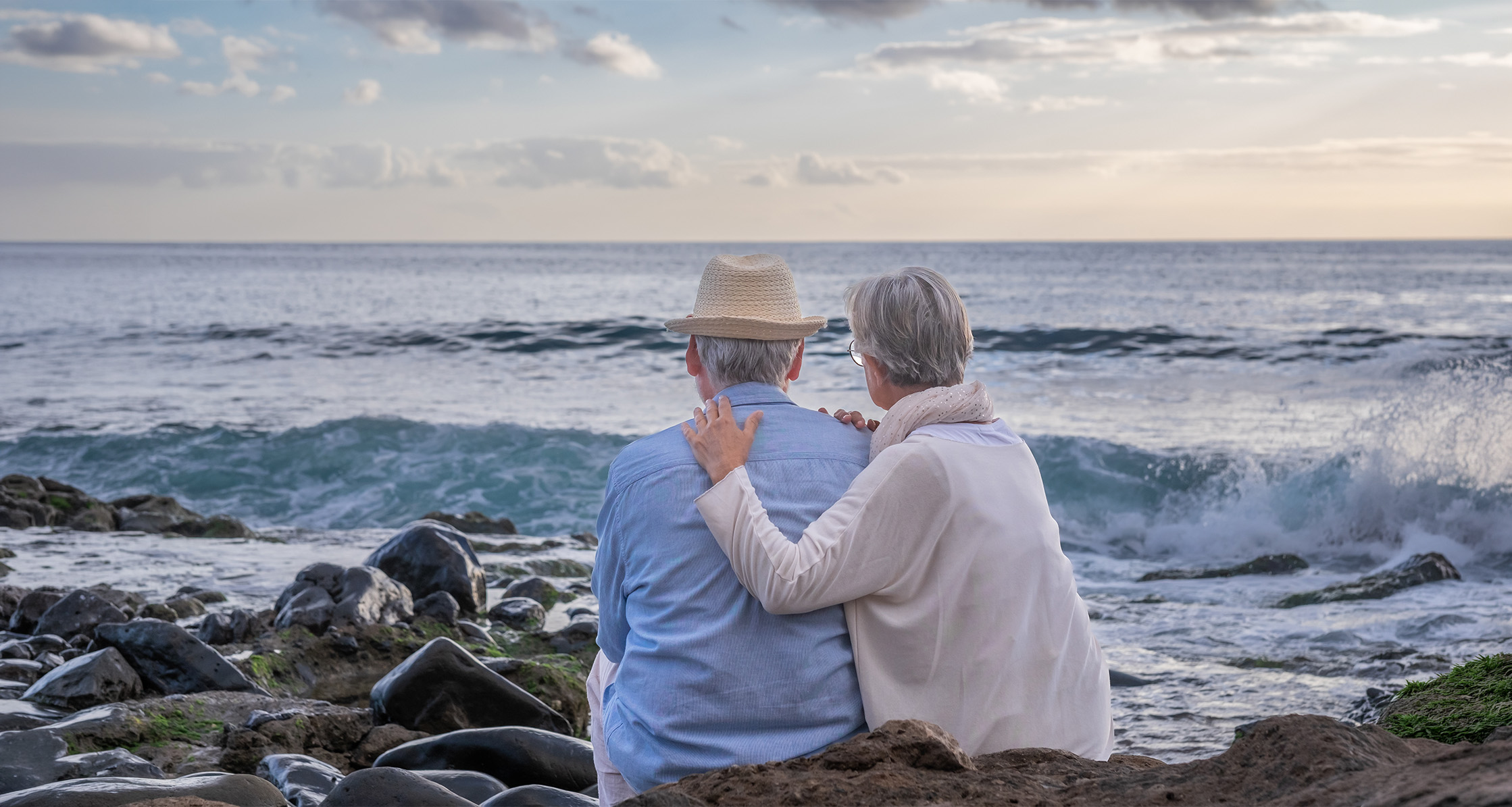 Retired couple embracing by the water at sunset.