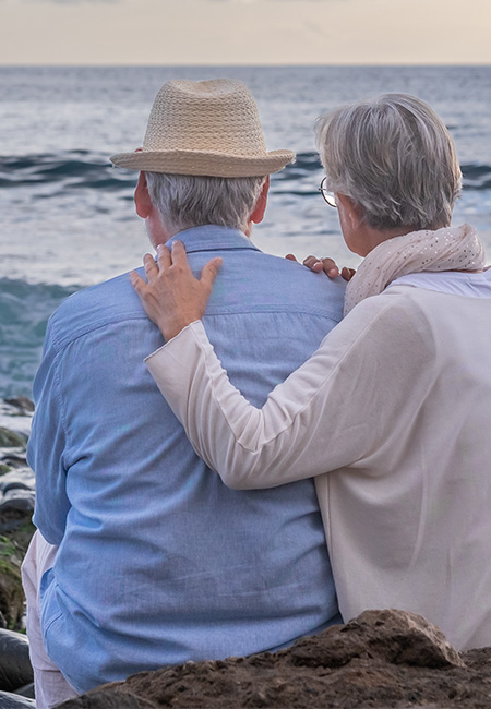 Retired couple embracing by the water at sunset.