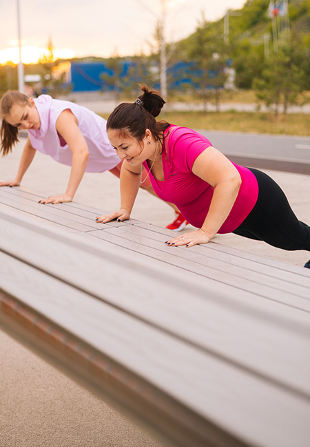 Two women performing incline push-ups outdoors.